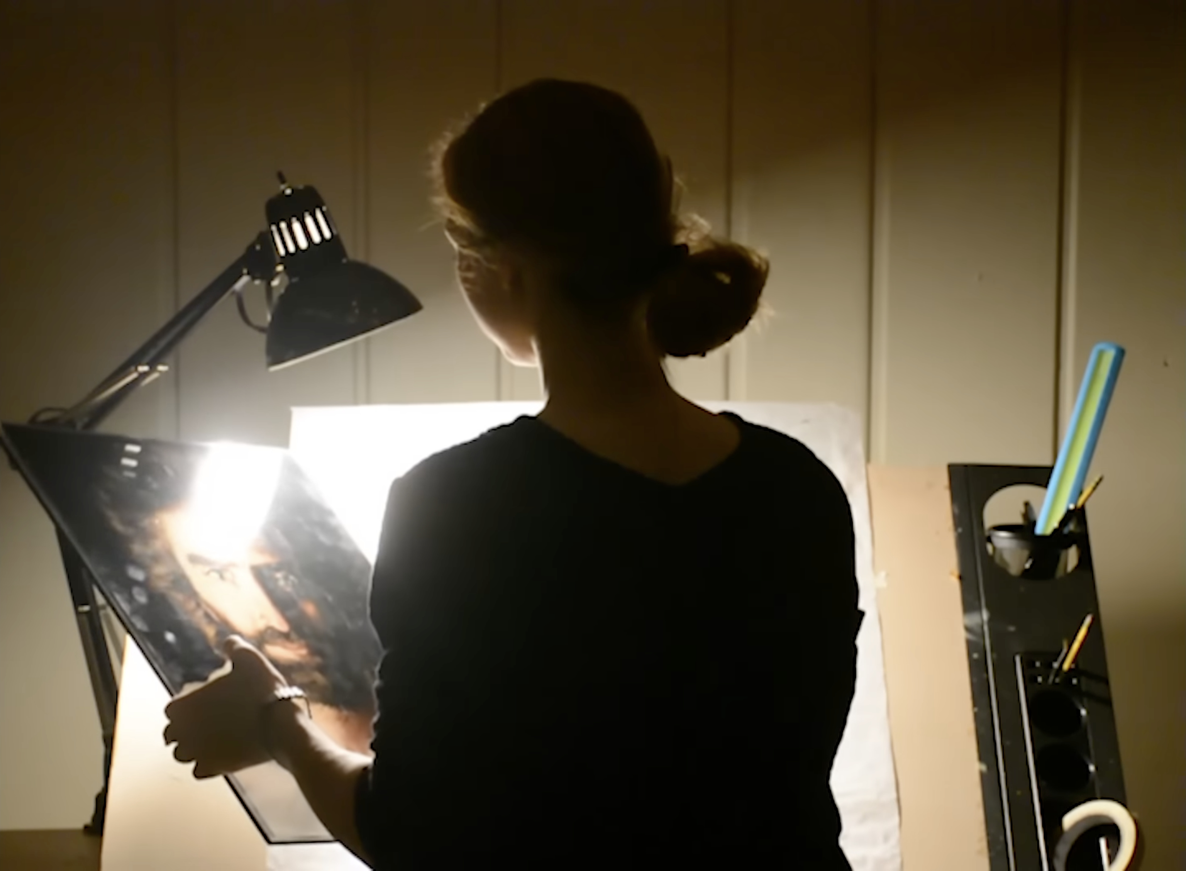 Akiane in silhouette holding a print of Prince of Peace under a lamp