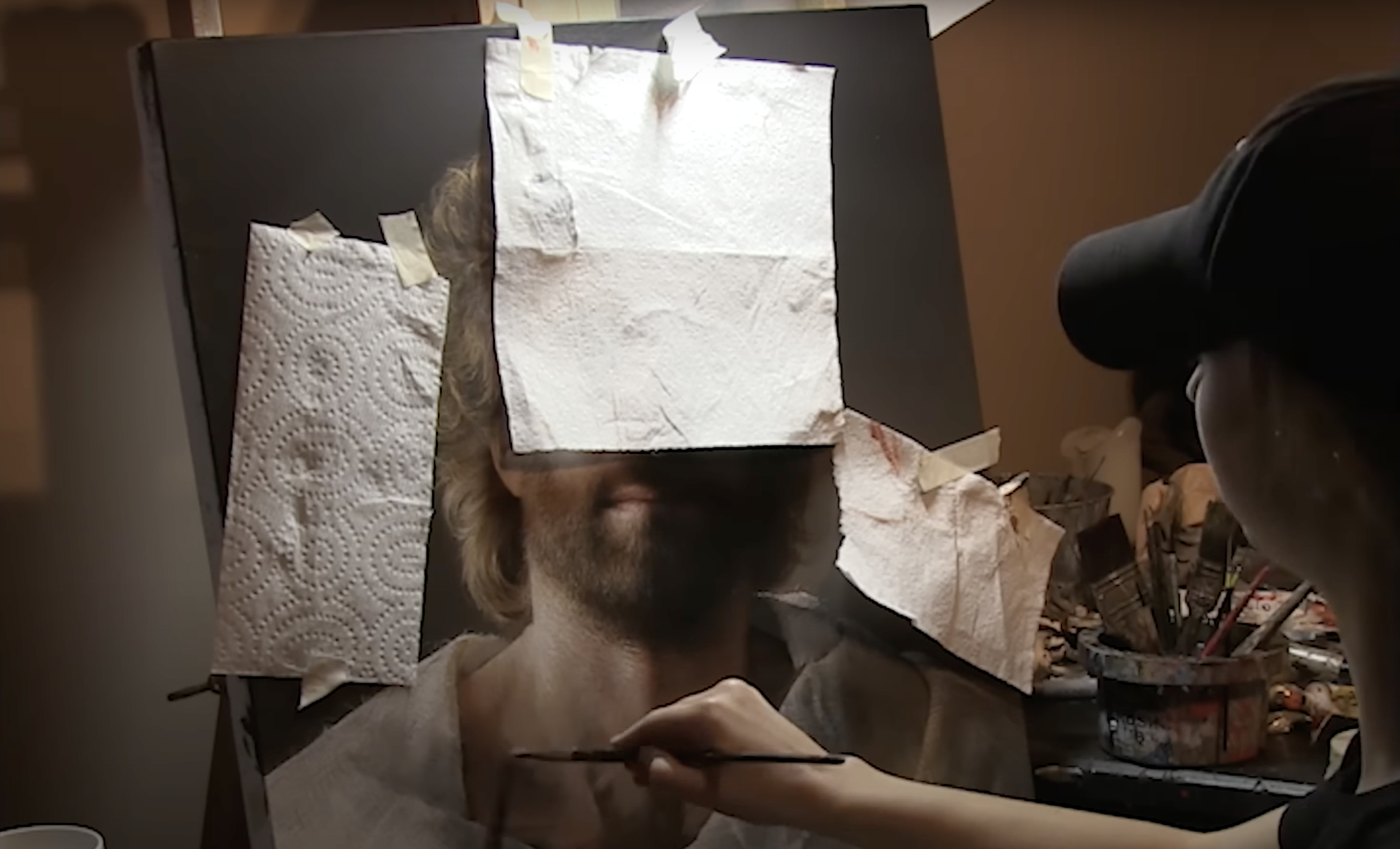 The portrait partly covered by taped paper towels as Akiane paints the lower face