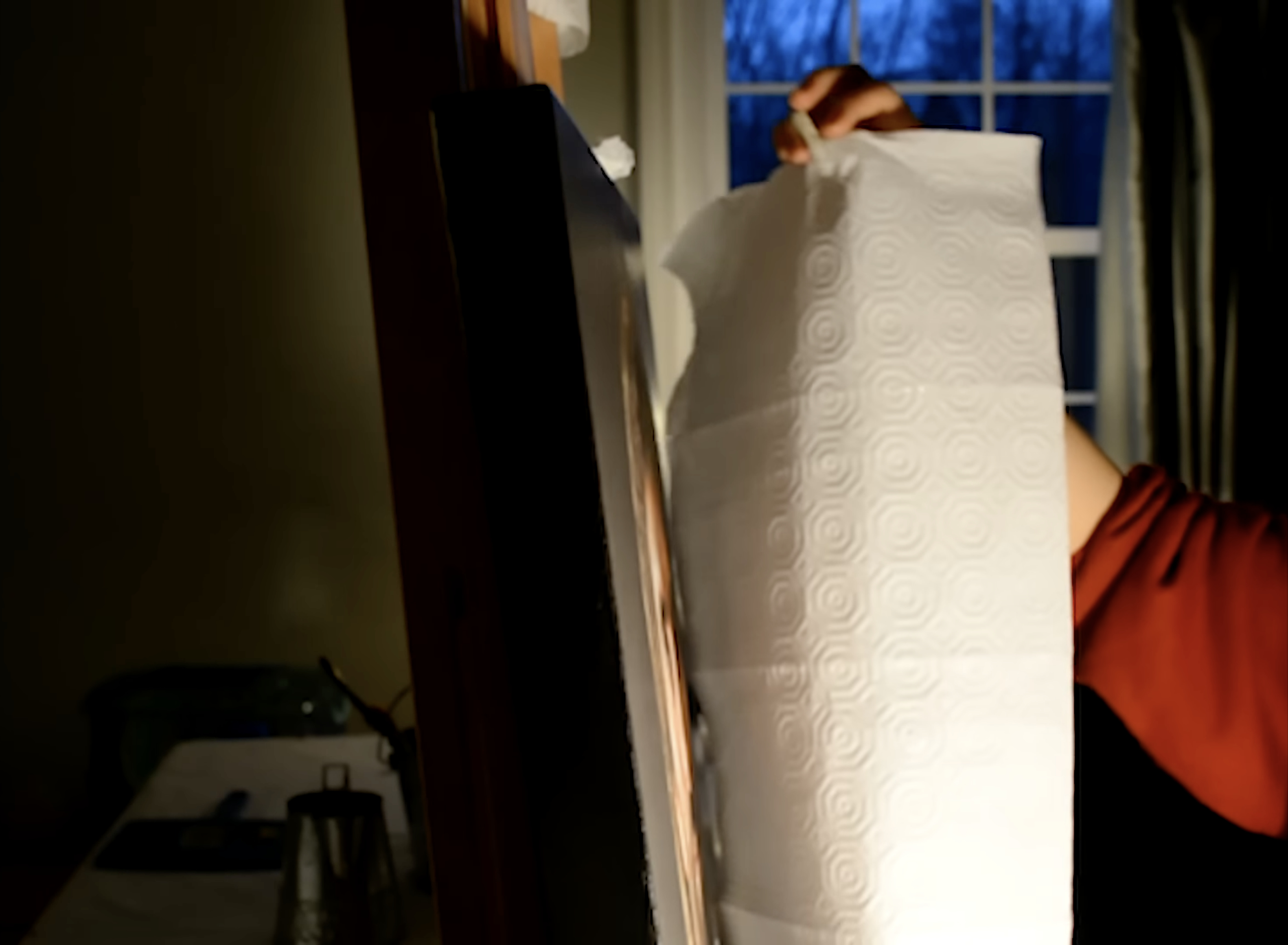 A hand lifting a sheet of paper towel from the canvas at night