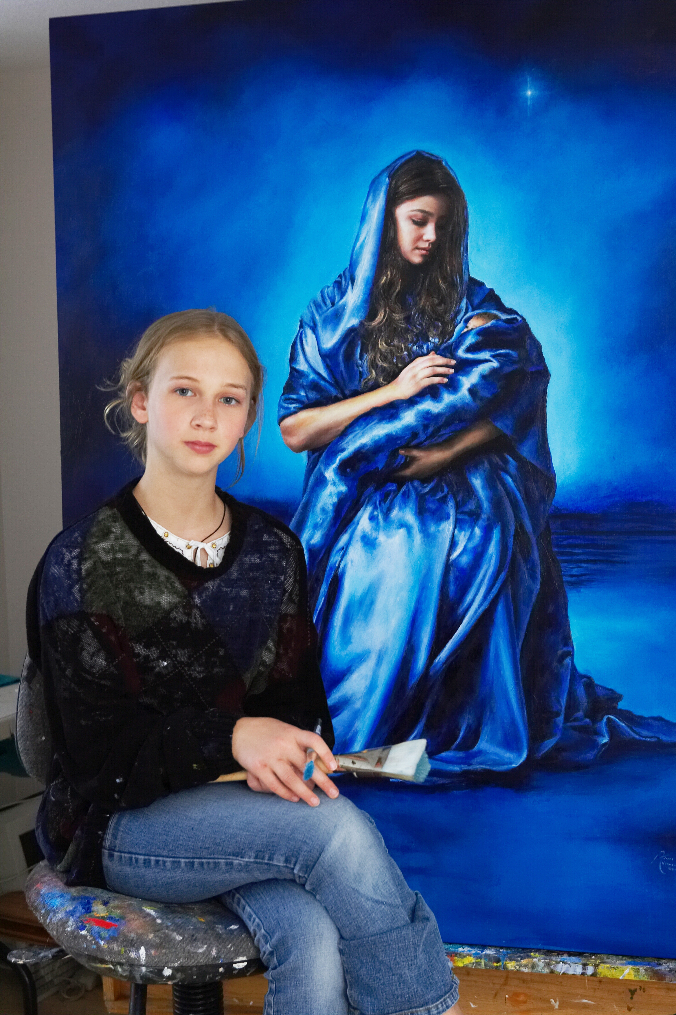 Akiane at age eleven seated before her painting of a mother holding her child